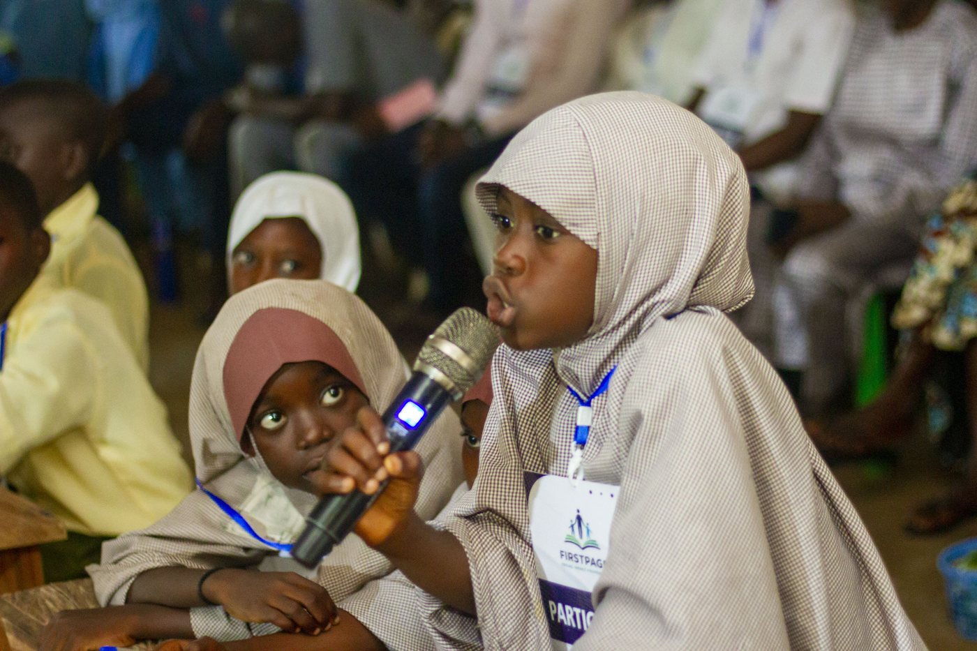 A FirstPage Foundation student speaking into a microphone during a debate session, with a fellow participant beside her